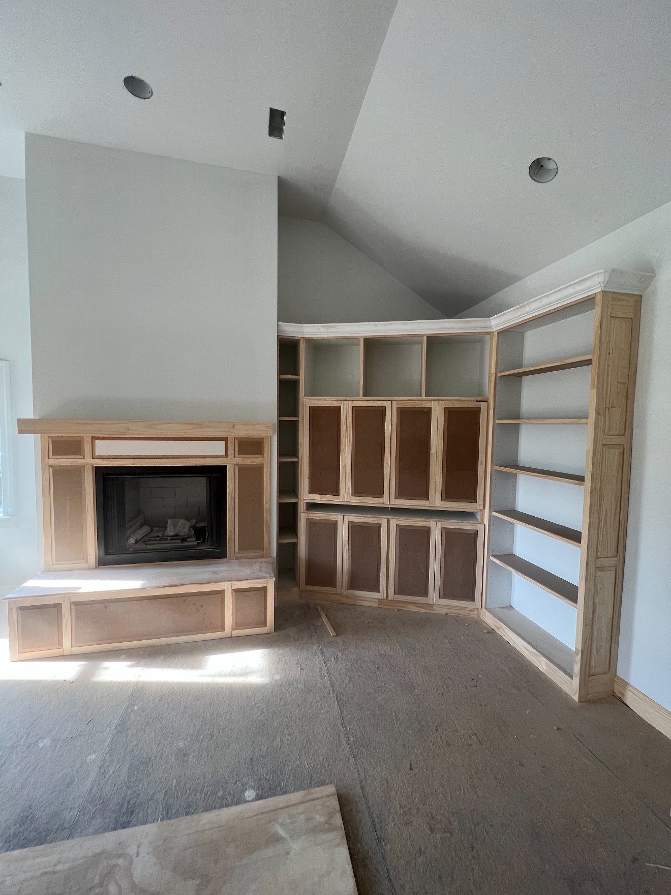 Custom fireplace surround and corner built-in cabinetry under construction in raw wood