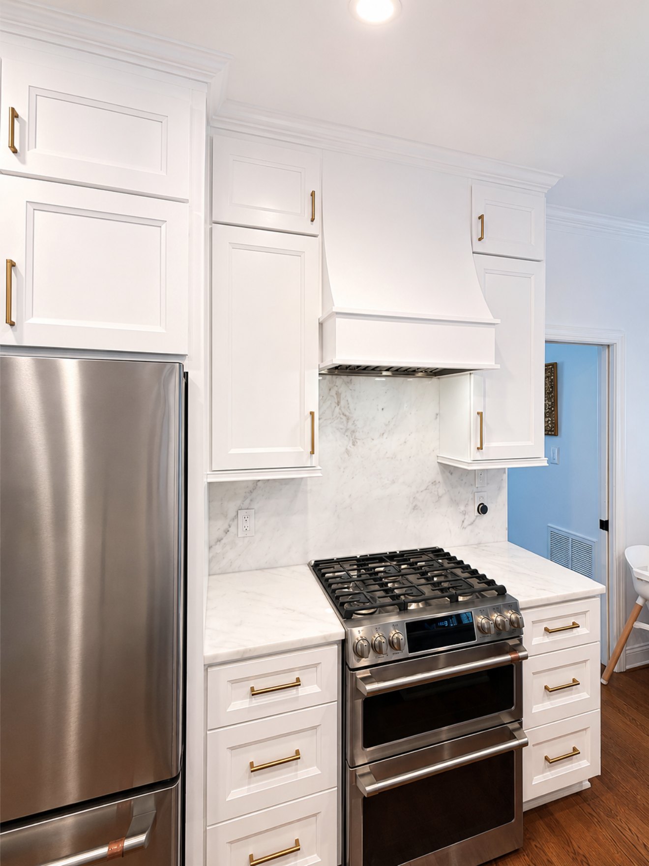 Finished kitchen detail showing custom range hood surround, marble backsplash, and brass hardware